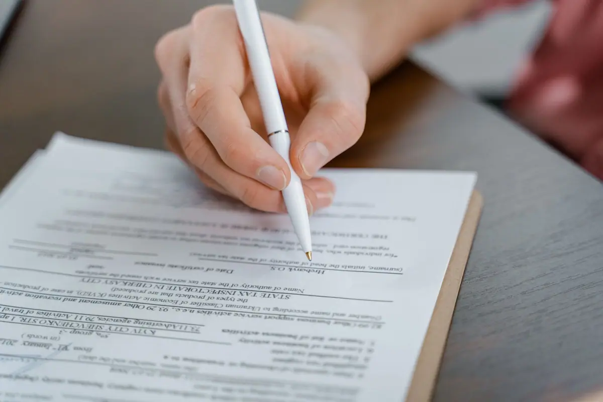 A hand signing a document with a pen