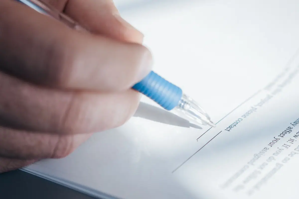 A hand with a pen signing a form