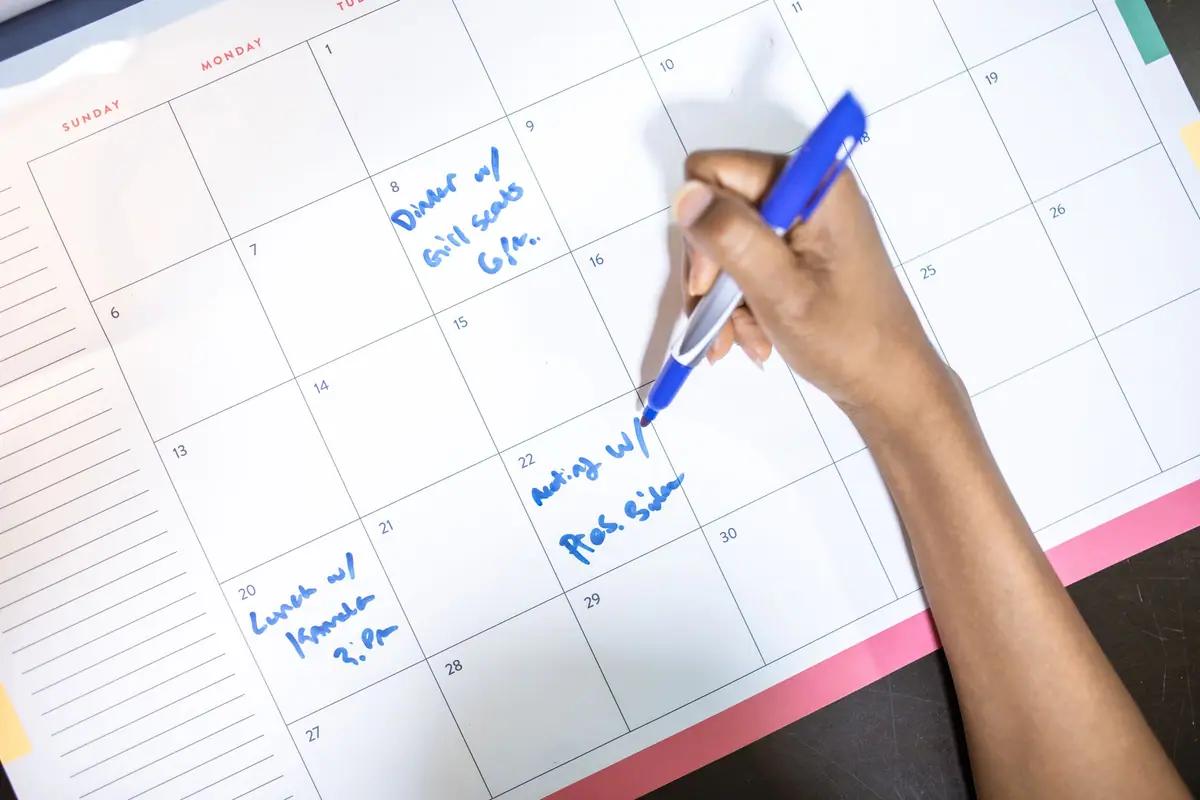 A hand writing appointments in a wall calendar