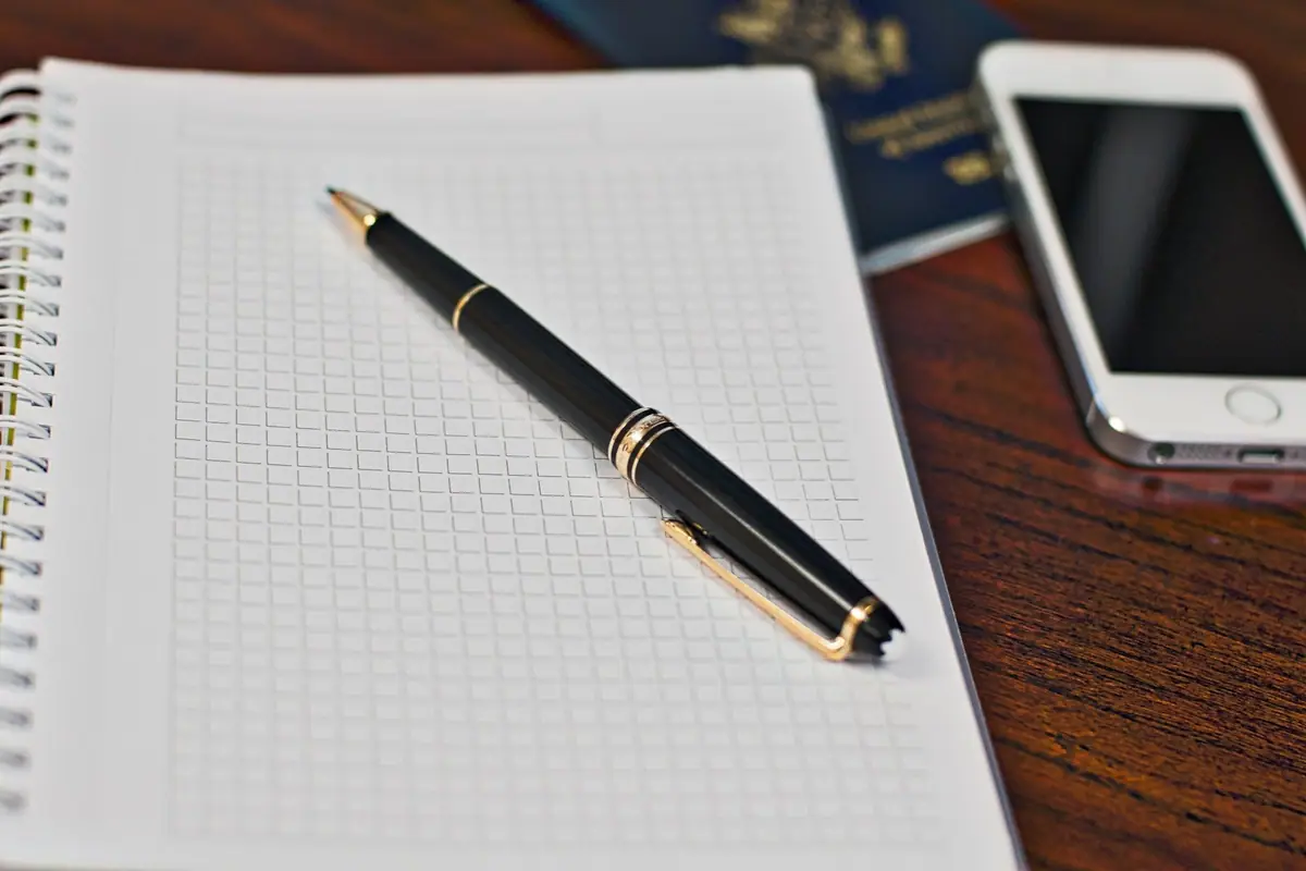 Passaporte, caderno, caneta e celular sobre uma mesa