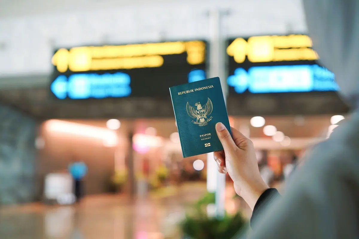 A traveller holding a passport in front of departure boards